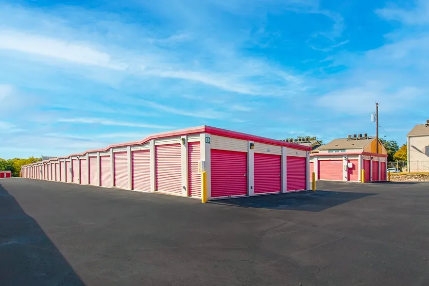 Drive-up storage units with red roll-up doors and wide asphalt access lanes